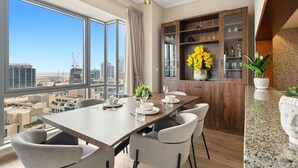 A modern dining area with a large table set for six, a view of the cityscape through large windows, and a wooden cabinet with glass doors. - Relaxing 1bedroom mins drive to Burj Khalifa (Dubai)