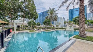 A swimming pool with lounge chairs, palm trees, and modern buildings in the background. - Relaxing 1bedroom mins drive to Burj Khalifa (Dubai)