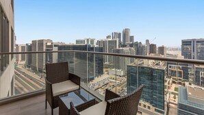 A balcony with wicker furniture and a glass table, overlooking a cityscape with modern buildings. - Relaxing 1bedroom mins drive to Burj Khalifa (Dubai)