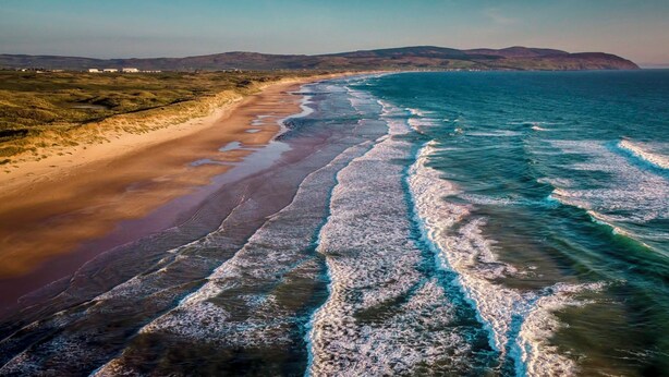 Paisatge costaner amb platja sorrenca i onades oceàniques.