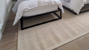 Ein Schlafzimmer mit zwei Betten, einem grünen Kopfteil, weißer Bettwäsche und einem gewebten Teppich.