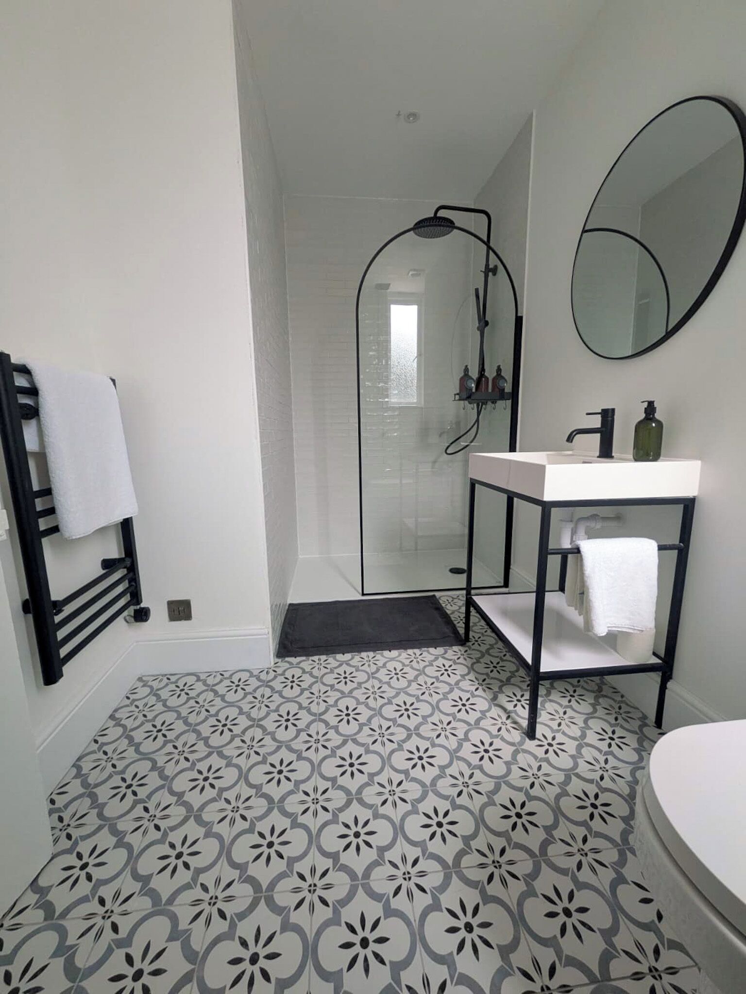 Ein Badezimmer mit Dusche, Waschbecken und Spiegel sowie Bodenfliesen mit Muster.