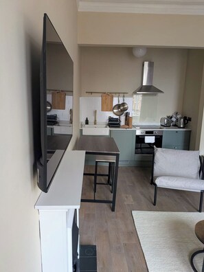 A modern kitchen with a flat-screen TV, a dining area with a table and chairs, and a large window.