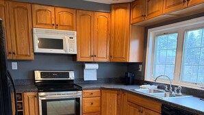 A kitchen with wooden cabinets, a microwave, a stove, a dishwasher, and a window with a view.