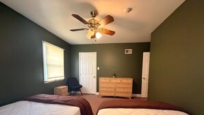 A bedroom with two beds, a ceiling fan, a dresser, and a chair.