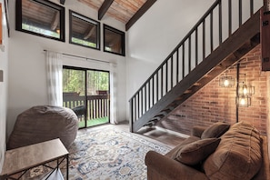A modern living room with a sofa, a small table, a patterned rug, a staircase with a wooden railing, and a brick wall.