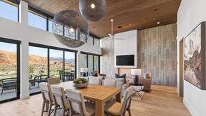 Un intérieur moderne comprenant un coin repas, des canapés, un téléviseur et une grande fenêtre donnant sur un paysage montagneux.