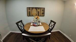Un comedor con una mesa redonda de madera, sillas negras, un jarrón con girasoles, un cuenco de bocadillos y un letrero que dice 'HOME' en la pared.