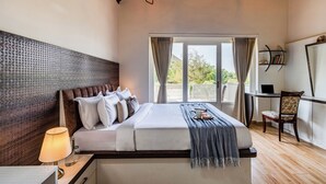 A bedroom with a bed, bedside table, lamp, chair, desk, laptop, and a view of greenery outside. - Alaya Stays Ramgarh Colonial 2BHK Villa (Jamwa Ramgarh)