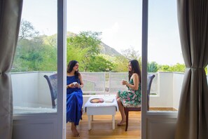 Two women seated at a table with a book and a tray of food, overlooking a mountainous landscape. - Alaya Stays Ramgarh Colonial 2BHK Villa (Jamwa Ramgarh)