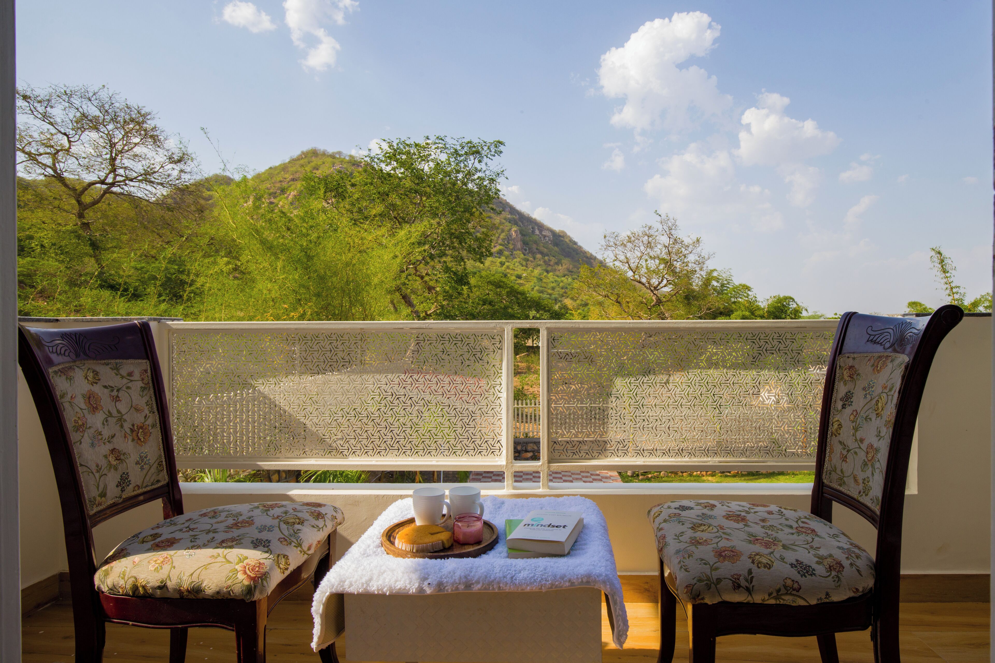 Un balcone con due sedie, un tavolo con un vassoio di cibo e vista su una montagna.