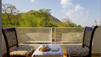 Un balcone con due sedie, un tavolo con un vassoio di cibo e vista su una montagna.
