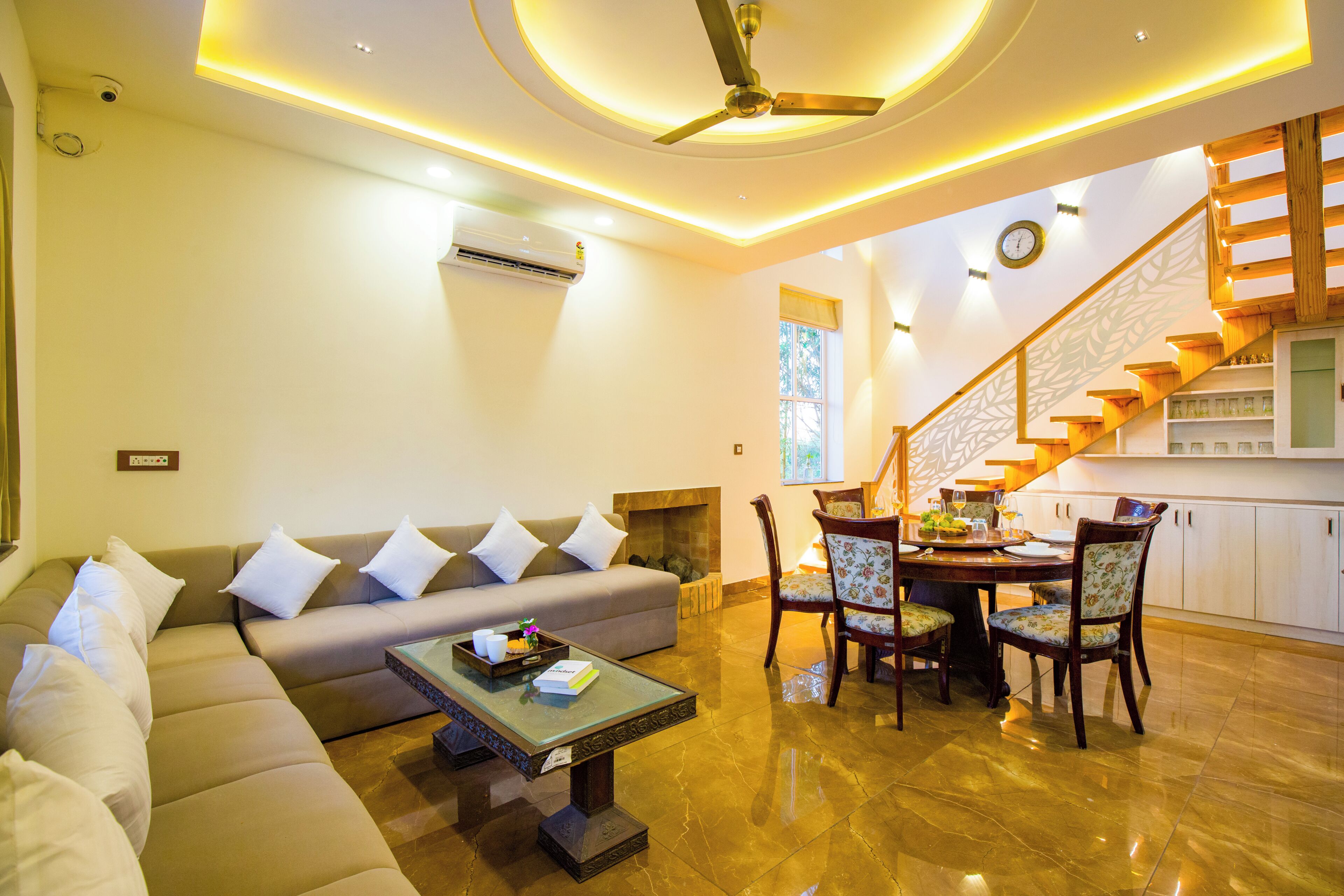 A modern living room with a sofa, coffee table, dining table with chairs, a ceiling fan, and a staircase.