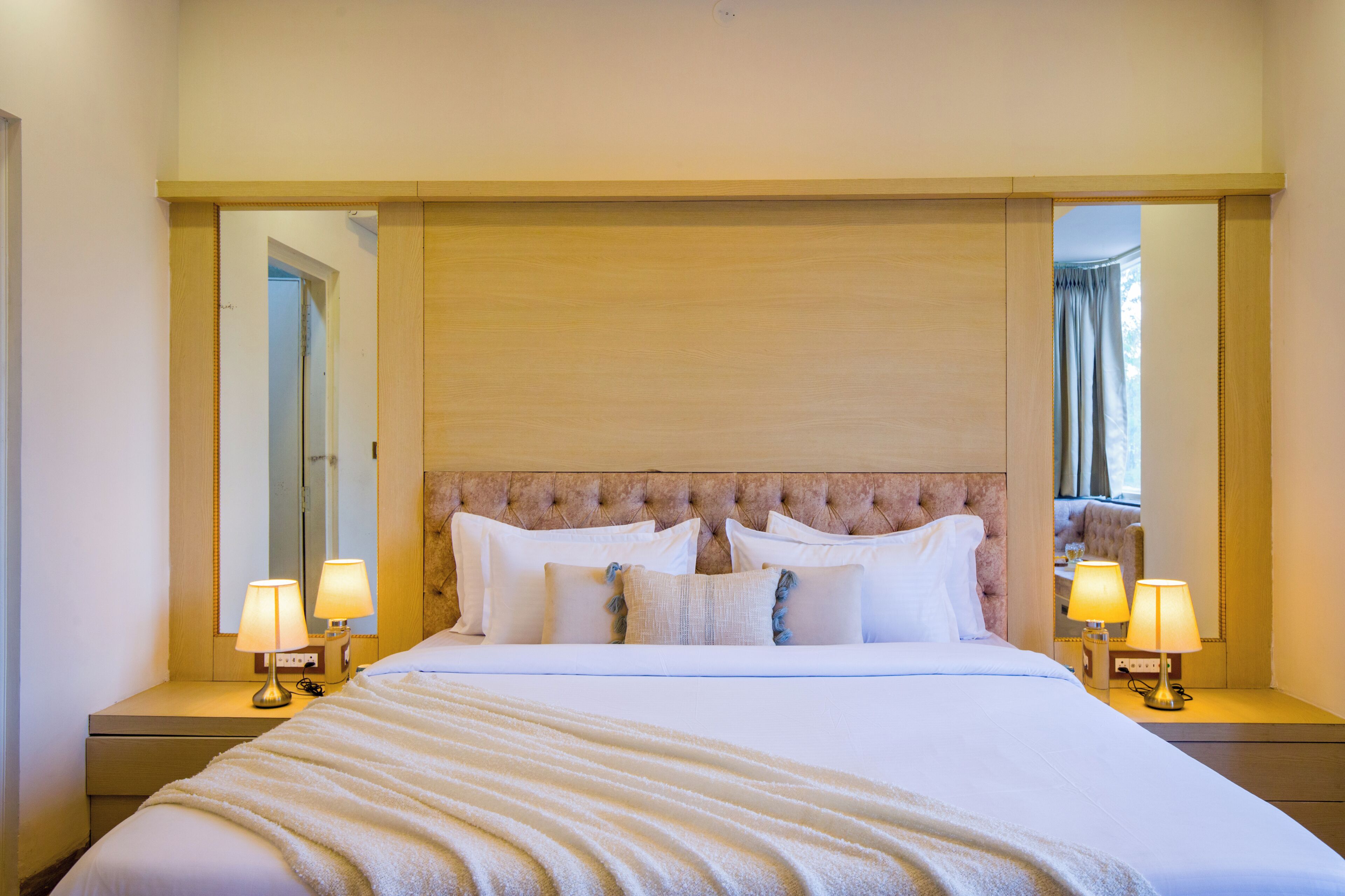 Habitación de hotel con una cama grande, dos lámparas de noche, un espejo y una ventana con cortinas.