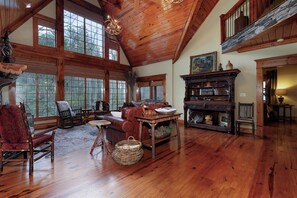 A spacious room with wooden floors, a large window, a fireplace, and a high ceiling. - The Lodge on Cartecay - Ellijay,GA (Ellijay)