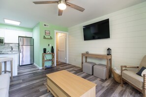 A modern kitchen with a stainless steel refrigerator, a wooden dining table, and a TV mounted on the wall. - 231 Breakers: Oceanfront Villa, 1BD/1BA/Sleeps 5 (Hilton Head Island)