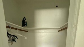 Ein kleiner, abgeschlossener Kleiderschrank mit Holzboden, weißer Wand und Deckenlüftung.
