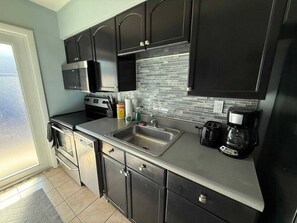 A modern kitchen with dark cabinetry, a stainless steel sink, and a coffee maker. - Cozy Haven Oasis: Pool| Los Olas |Wilton Manors (Wilton Manors)