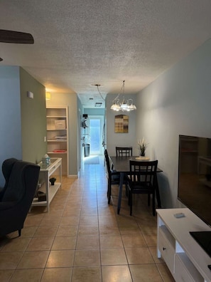 A modern living room with a black chair, a dining table with chairs, a TV, and a kitchen area with a chandelier. - Cozy Haven Oasis: Pool| Los Olas |Wilton Manors (Wilton Manors)