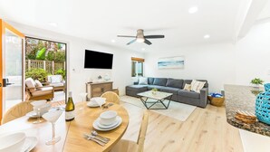 A modern living room with a dining area, a gray sofa, a ceiling fan, and a TV mounted on the wall. - Amazing Location, Across from the Beach W/Jacuzzi! (San Diego)