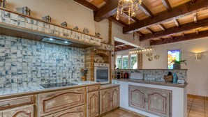 A kitchen with exposed brick walls, wooden beams, and a tiled backsplash. - Languedoc Villa with Pool and Mountain View (Pailhès)