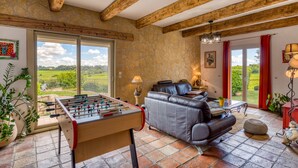 A room with a foosball table, leather sofa, stone wall, and large windows. - Languedoc Villa with Pool and Mountain View (Pailhès)