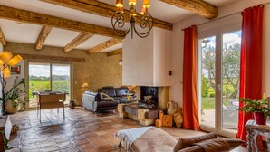 A spacious living area with a fireplace, a sofa, a table, and a view of the outdoors. - Languedoc Villa with Pool and Mountain View (Pailhès)