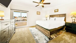 Ein Schlafzimmer mit Bett, Deckenventilator, Nachttischlampen, einem Schminktisch und Blick durch eine Schiebetür.