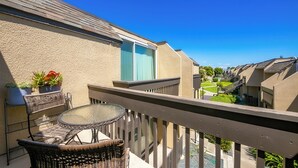 Ein Balkon mit Korbmöbeln, einem Glastisch und Topfpflanzen.