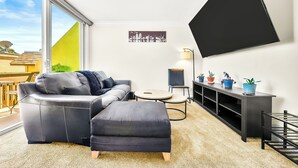 Ein modernes Wohnzimmer mit einer Couch, einem Hocker und einem an der Wand befestigten Flachbildfernseher.