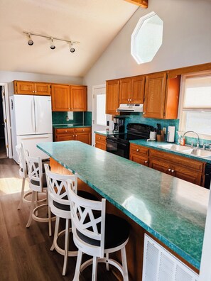 Une cuisine moderne avec des meubles en bois, un grand îlot central doté de tabourets, un réfrigérateur et une cuisinière.