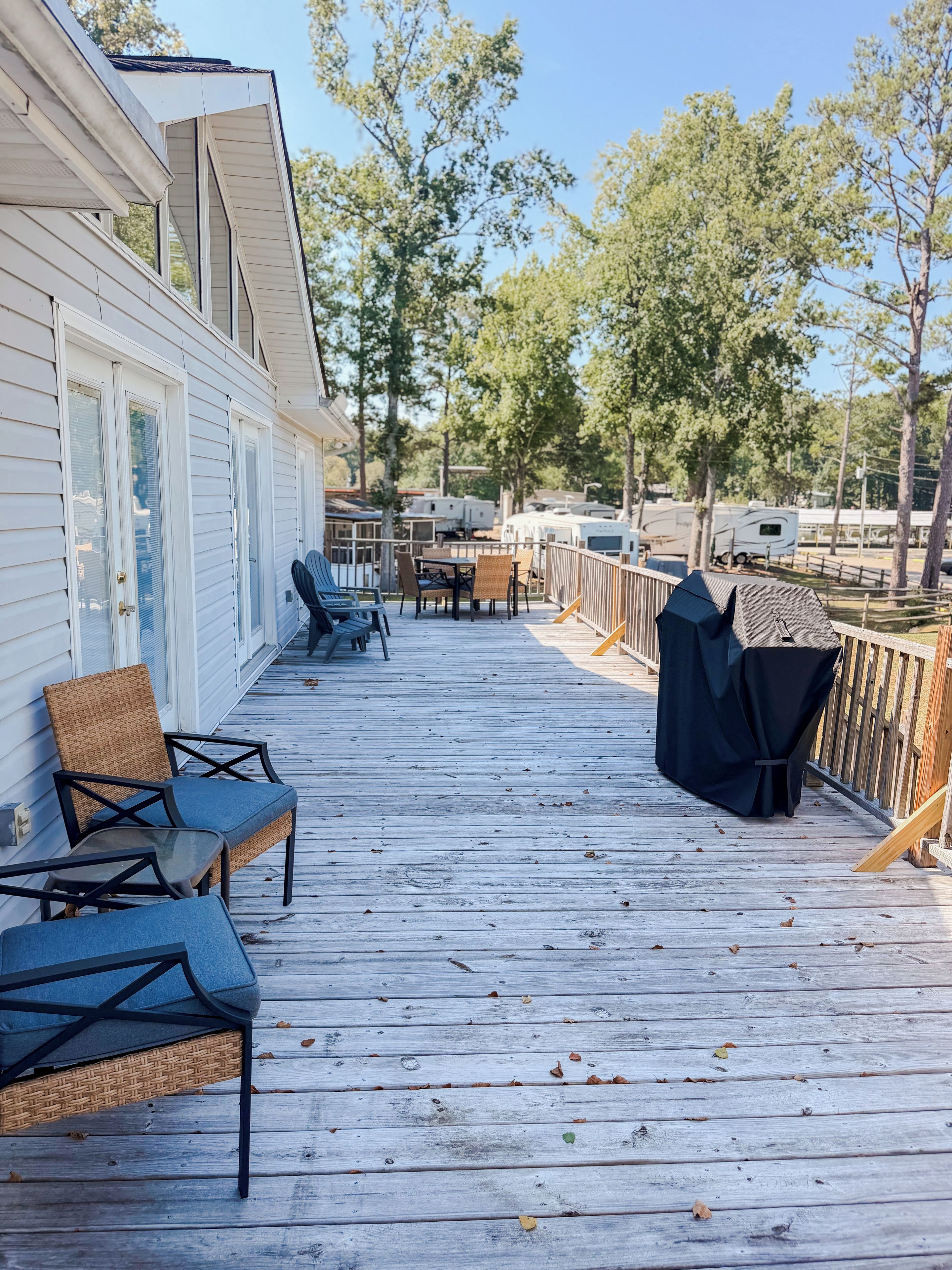 Une terrasse en bois, dotée de mobilier d’extérieur et d’un barbecue, qui offre une vue sur un terrain de camping.