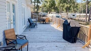 Une terrasse en bois, dotée de mobilier d’extérieur et d’un barbecue, qui offre une vue sur un terrain de camping.