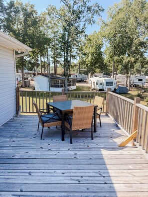 Une terrasse avec une table et des chaises, entourée d’une rambarde en bois, donnant sur un terrain de camping avec des camping-cars et des arbres.