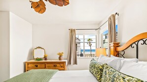 Een hotelkamer met een bed, een houten dressoir, een spiegel, een raam met uitzicht op het strand en een balkon.
