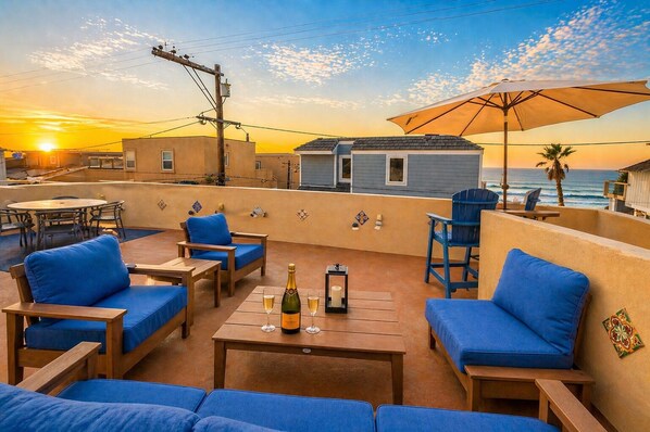 A rooftop terrace with outdoor seating, a table with a bottle and glasses, and a view of the ocean at sunset. - Great Reviews, Large Rooftop Deck W/Parking, Stunning (San Diego)
