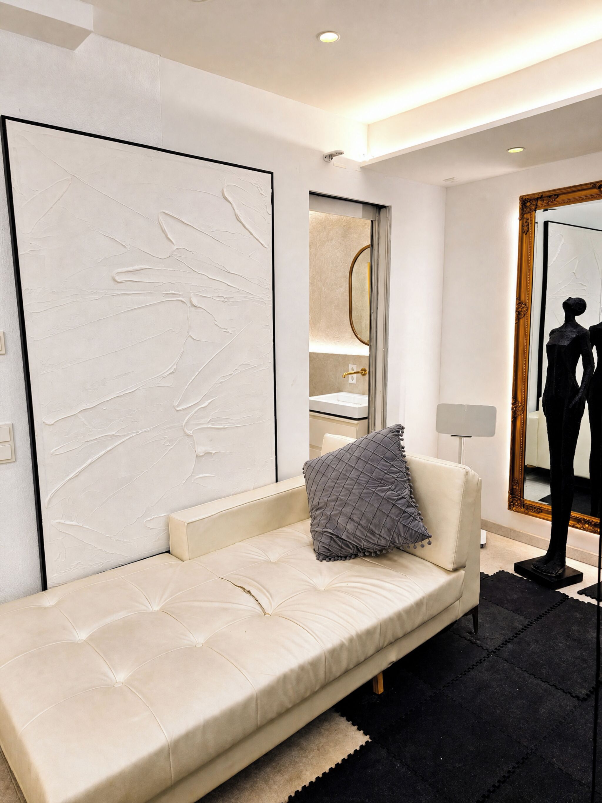 Ein modernes Wohnzimmer mit einem weißen Sofa, einer großen abstrakten Wandkunst, einem Spiegel mit goldener Rahmen und einer schwarz-weißen Mannequin.