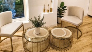 A modern room with a large window, a flat-screen TV, two chairs, a round coffee table, and a potted plant.