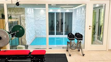 Ein Heimfitnessraum mit Langhantelbank, Kniebeugestange und Gewichtsplatten mit Blick auf einen Swimmingpool.