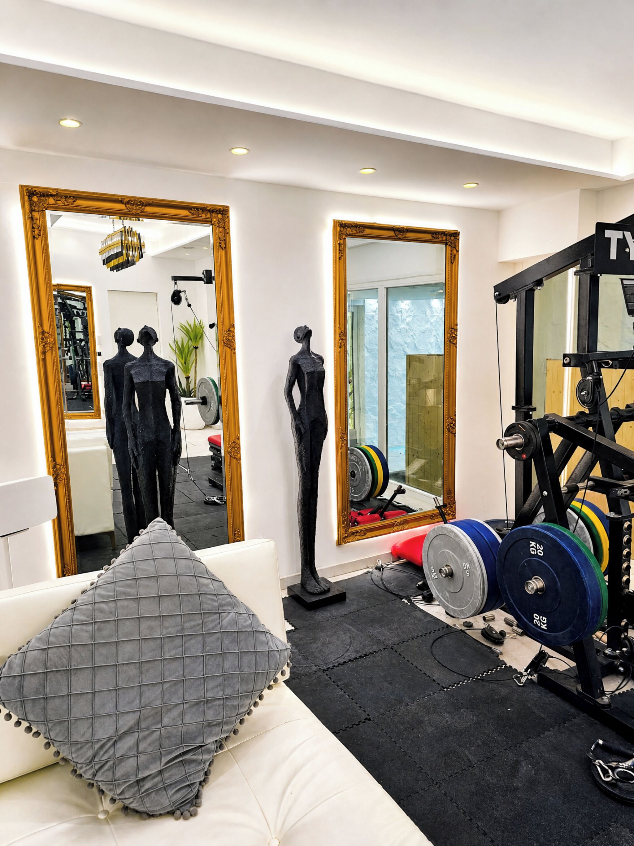 A gym with exercise equipment, a mirror, and a sofa with a cushion.