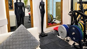 A gym with exercise equipment, a mirror, and a sofa with a cushion.