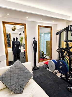 Ett gym med träningsredskap, en spegel och en soffa med en kudde.