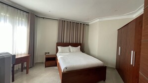 Une chambre d’hôtel avec un lit en bois, un bureau, une armoire et une fenêtre avec des rideaux.