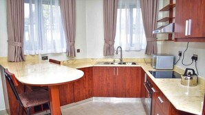 Une cuisine dotée d’un plan de travail en marbre, de meubles en bois, d’un évier, d’un four à micro-ondes et d’une bouilloire.
