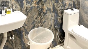 A bathroom with a marble wall, a round mirror, a white sink, a toilet, and a shower area. - Hotel Girraj Stay Inn  (Mathura)