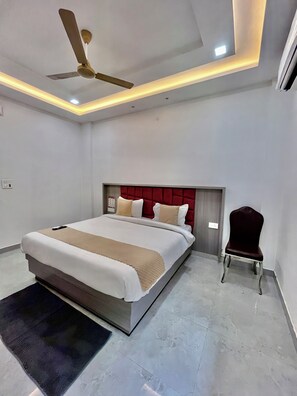 A modern bedroom with a bed, a chair, a ceiling fan, and recessed lighting. - Hotel Girraj Stay Inn  (Mathura)
