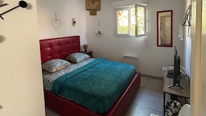 A bedroom with a red bed, a desk with a computer, a window, and a hanging light fixture. - Mini Villa "Mon Rêve Corse" Seaside in Residence with Swimming Pool (Cervione)