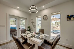 A dining area with a table set for four, chairs, a clock on the wall, and a view of the outdoors. - Villa Sunnyside Up- Your Peaceful Getaway in NW Cape Coral (Cape Coral)
