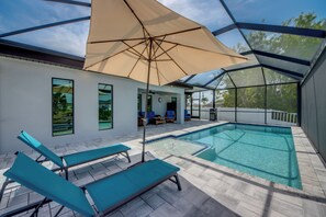A swimming pool with lounge chairs and a large umbrella, surrounded by a covered patio area. - Villa Sunnyside Up- Your Peaceful Getaway in NW Cape Coral (Cape Coral)