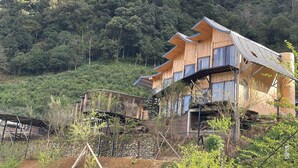Una cabaña de madera con varios balcones, rodeada por un muro de piedra y abundante vegetación.